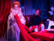 Queen Elizabeth sits on a couch with Halston and admires a piece of red fabric
